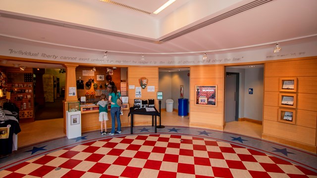 A red and white tile floor in an oval room with two people standing at a desk speaking to a ranger